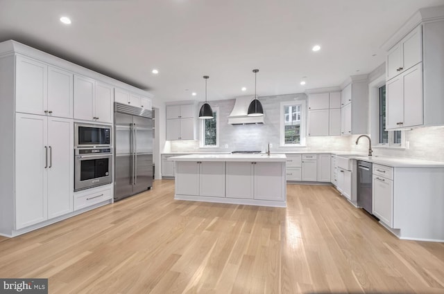 kitchen with a kitchen island, decorative light fixtures, white cabinetry, built in appliances, and custom range hood