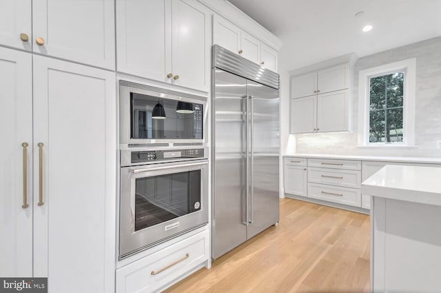 kitchen with white cabinetry, built in appliances, light wood-type flooring, and decorative backsplash