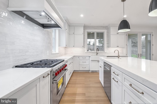 kitchen with stainless steel appliances, light stone countertops, custom range hood, white cabinets, and decorative light fixtures