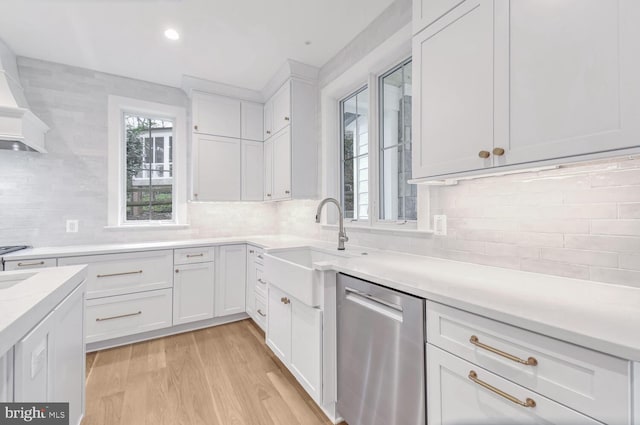 kitchen featuring sink, dishwasher, white cabinets, light hardwood / wood-style floors, and wall chimney range hood