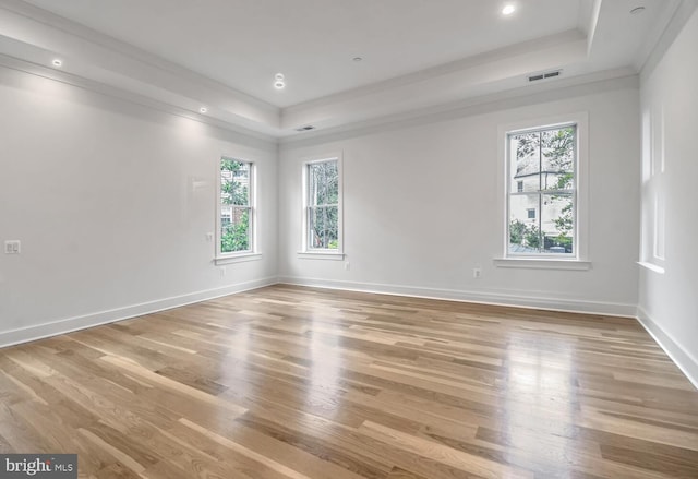 empty room with a tray ceiling, ornamental molding, and light hardwood / wood-style floors