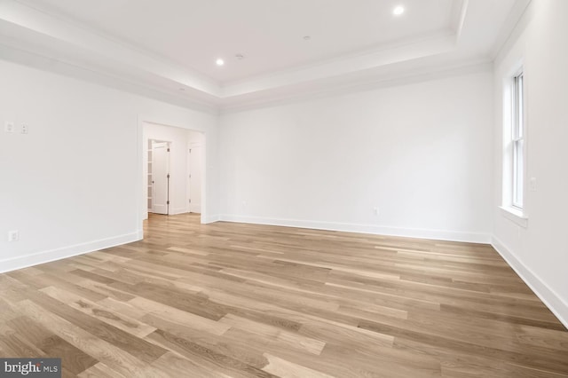 spare room featuring ornamental molding, a raised ceiling, and light wood-type flooring