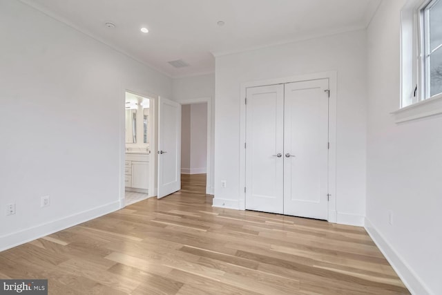 unfurnished bedroom featuring ornamental molding, connected bathroom, light wood-type flooring, and a closet