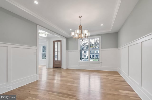 unfurnished dining area featuring a notable chandelier, a tray ceiling, light hardwood / wood-style flooring, and ornamental molding