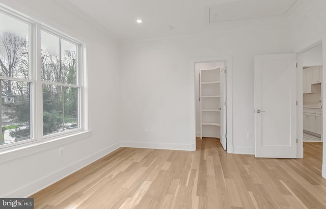 unfurnished bedroom with multiple windows, a walk in closet, light wood-type flooring, and a closet