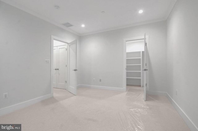 unfurnished bedroom with crown molding, a walk in closet, and light carpet