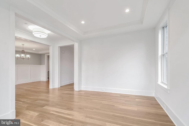 empty room with crown molding, a chandelier, a raised ceiling, and light wood-type flooring