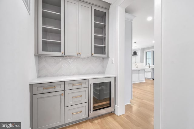 bar featuring wine cooler, gray cabinets, tasteful backsplash, and light wood-type flooring