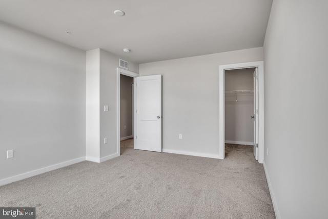 unfurnished bedroom with a spacious closet, visible vents, baseboards, and carpet floors