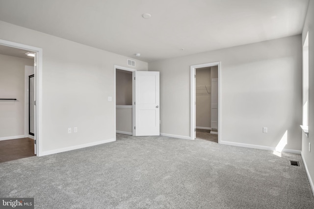 unfurnished bedroom featuring baseboards, visible vents, a walk in closet, and carpet flooring