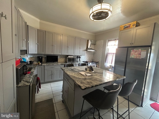 kitchen featuring dark stone countertops, ornamental molding, a kitchen island, stainless steel appliances, and wall chimney range hood