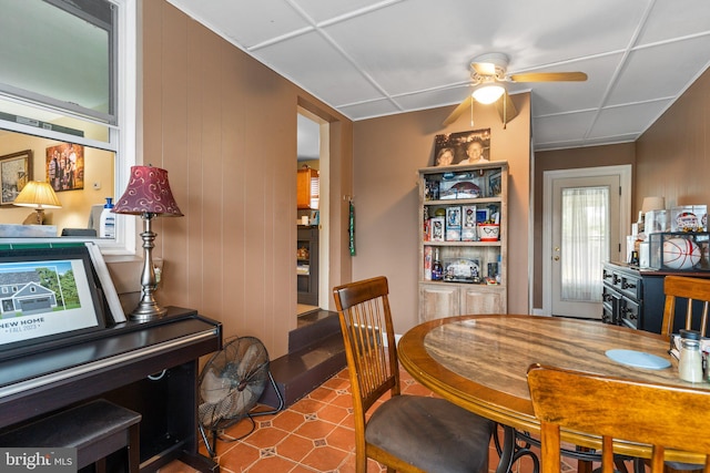 dining space featuring a drop ceiling, ceiling fan, and wood walls