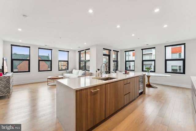 kitchen with sink, light hardwood / wood-style flooring, beverage cooler, and a center island with sink