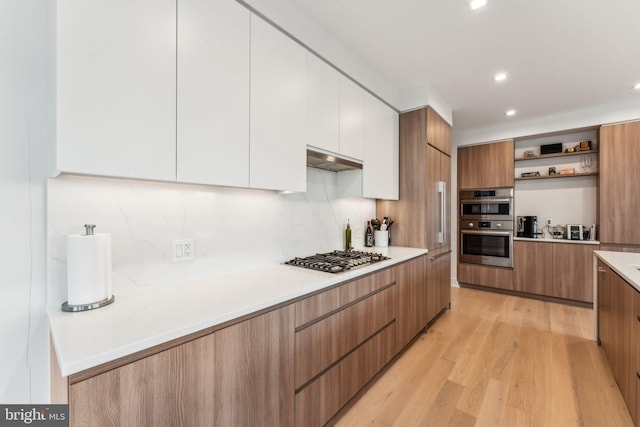 kitchen with stainless steel appliances, white cabinets, backsplash, and light hardwood / wood-style flooring