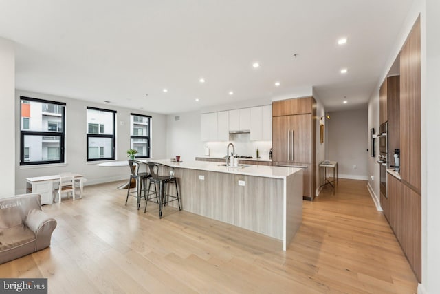 kitchen featuring a breakfast bar area, paneled built in fridge, white cabinets, a large island with sink, and light wood-type flooring