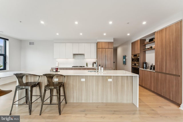 kitchen with white cabinetry, sink, a large island, stainless steel gas cooktop, and light wood-type flooring