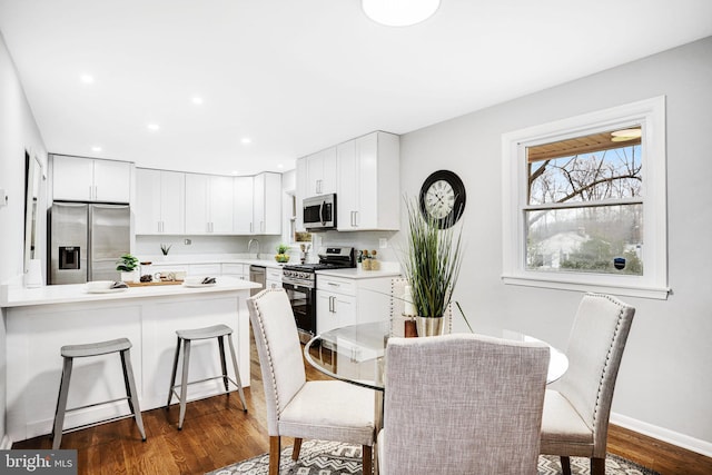 kitchen featuring stainless steel appliances, white cabinetry, dark hardwood / wood-style floors, and a kitchen bar