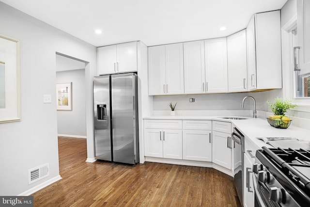 kitchen with wood-type flooring, appliances with stainless steel finishes, sink, and white cabinets