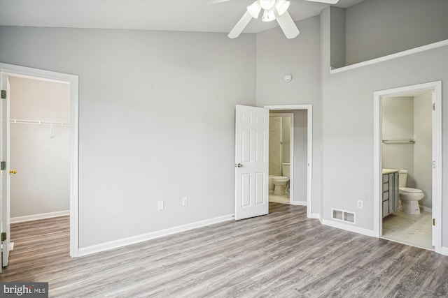 unfurnished bedroom featuring a towering ceiling, connected bathroom, a spacious closet, light hardwood / wood-style floors, and a closet