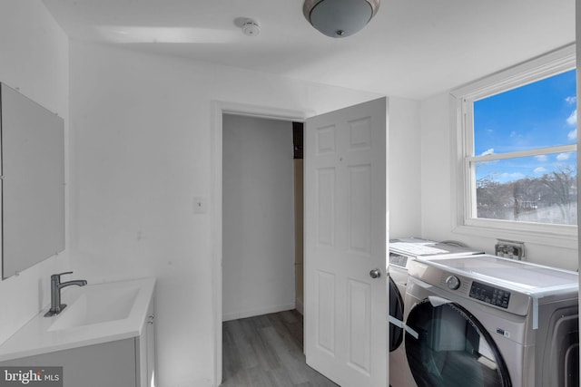 clothes washing area featuring washing machine and dryer, sink, and light hardwood / wood-style floors