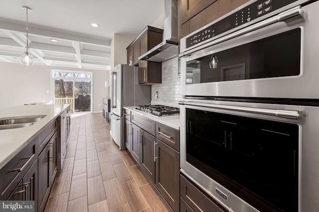 kitchen featuring wall chimney range hood, appliances with stainless steel finishes, hanging light fixtures, coffered ceiling, and decorative backsplash