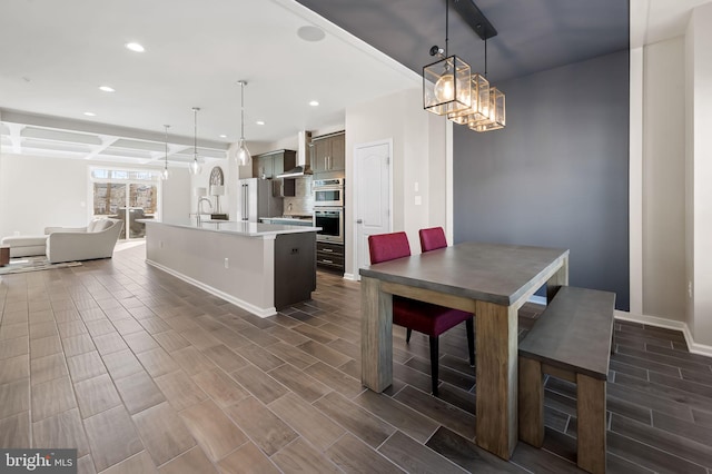 interior space featuring pendant lighting, wall chimney exhaust hood, appliances with stainless steel finishes, and a kitchen island with sink