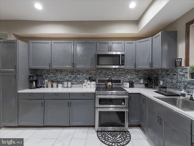 kitchen with stainless steel appliances, gray cabinets, sink, and decorative backsplash