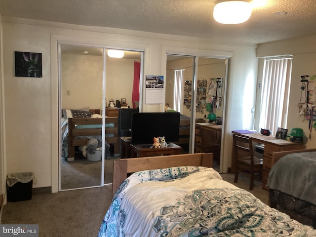 bedroom with multiple closets, a textured ceiling, and dark carpet