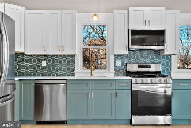 kitchen featuring plenty of natural light, stainless steel appliances, decorative backsplash, white cabinets, and decorative light fixtures