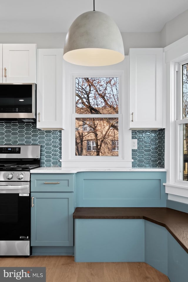 kitchen with appliances with stainless steel finishes, pendant lighting, tasteful backsplash, white cabinetry, and blue cabinetry