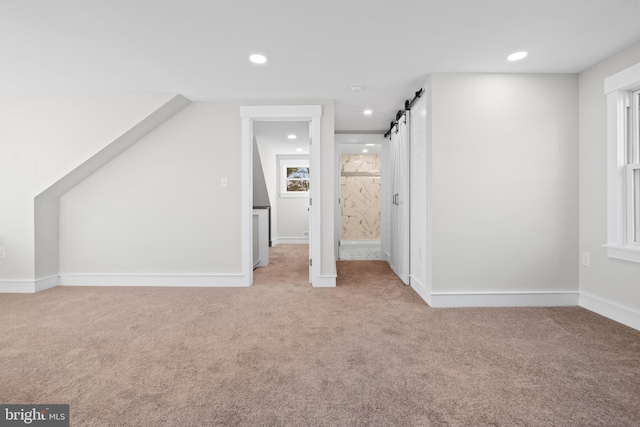 additional living space featuring light colored carpet and a barn door