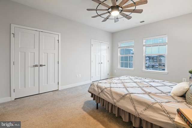 bedroom featuring light carpet, baseboards, visible vents, and two closets