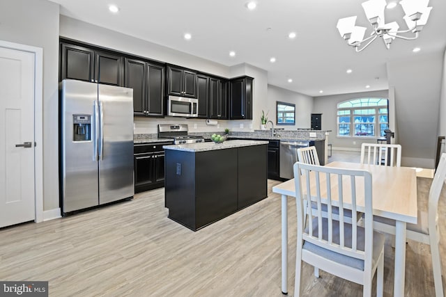 kitchen featuring light wood finished floors, stainless steel appliances, recessed lighting, a kitchen island, and dark cabinets