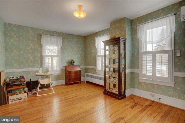 sitting room featuring a wall unit AC, radiator heating unit, and wood-type flooring