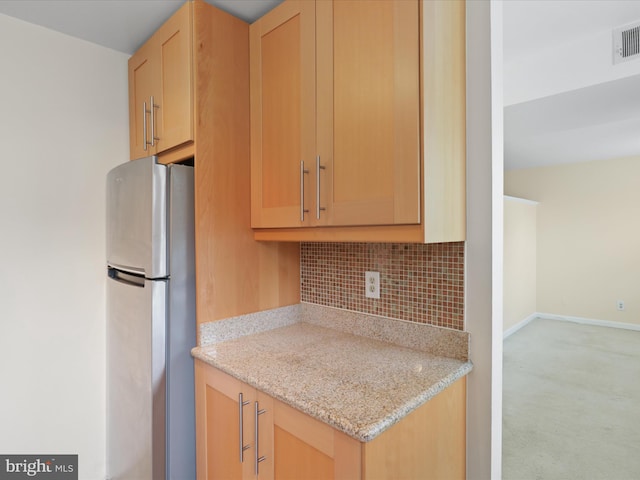 kitchen featuring backsplash, light brown cabinets, stainless steel fridge, light stone counters, and light carpet