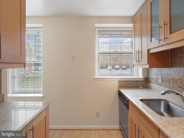 kitchen featuring tasteful backsplash, sink, stainless steel dishwasher, light stone countertops, and light wood-type flooring