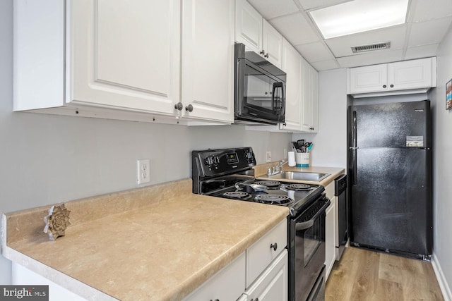 kitchen featuring sink, white cabinetry, black appliances, light wood-type flooring, and a drop ceiling