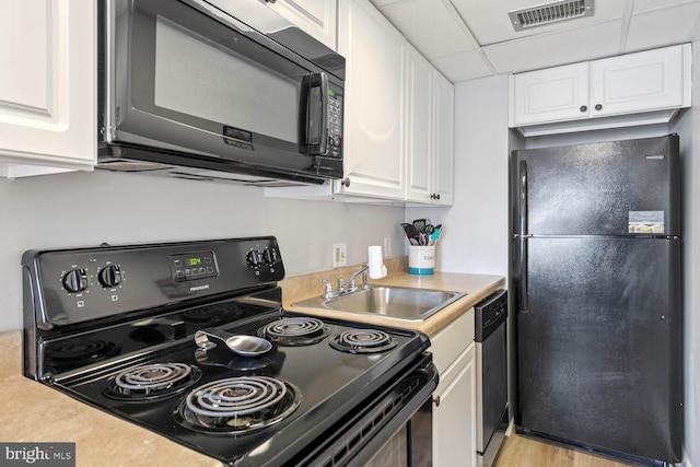 kitchen with a drop ceiling, sink, black appliances, and white cabinets