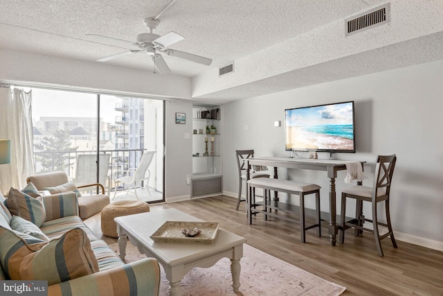 living room featuring ceiling fan, light hardwood / wood-style flooring, and a textured ceiling