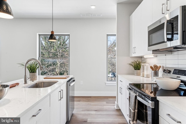 kitchen with pendant lighting, sink, white cabinetry, stainless steel appliances, and light stone countertops