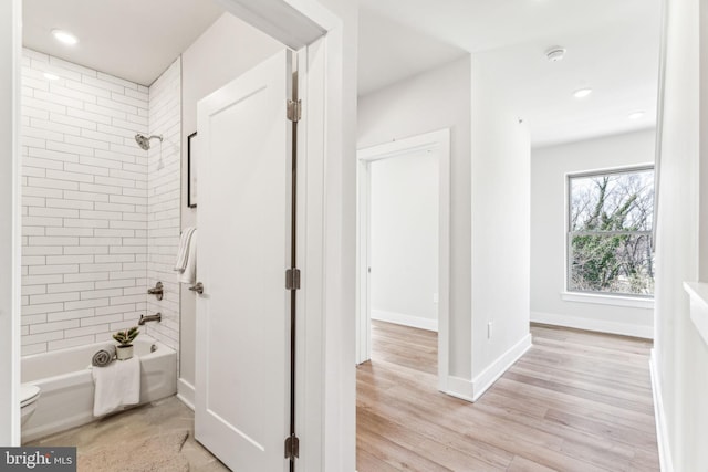 bathroom with tiled shower / bath combo, wood-type flooring, and toilet