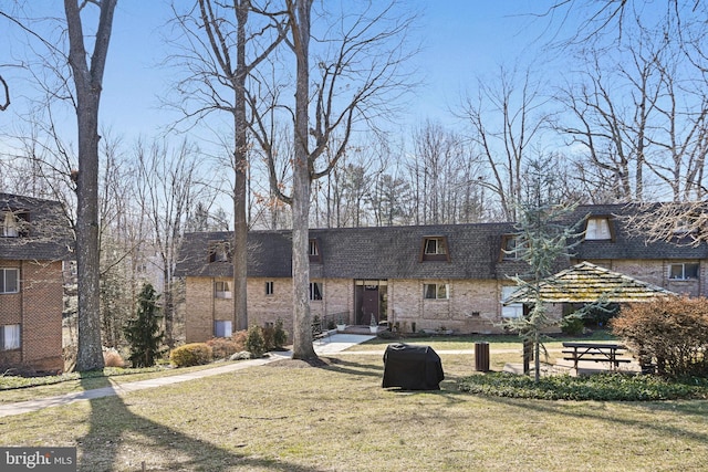 view of front of house with a front lawn, a shingled roof, mansard roof, and brick siding
