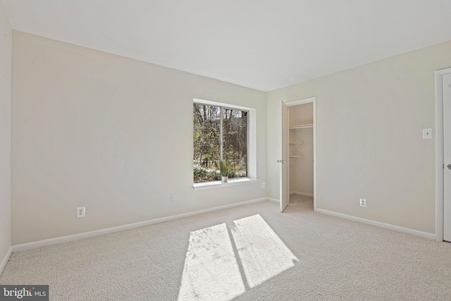unfurnished bedroom featuring baseboards, a closet, light colored carpet, and a spacious closet