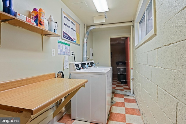 laundry area with concrete block wall, washer and dryer, and light floors