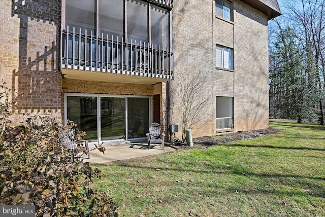 back of house featuring a lawn, brick siding, a patio, and a balcony