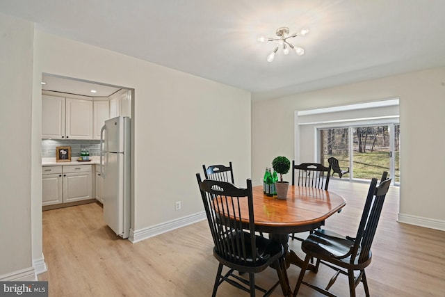 dining space with baseboards, light wood-style flooring, and an inviting chandelier
