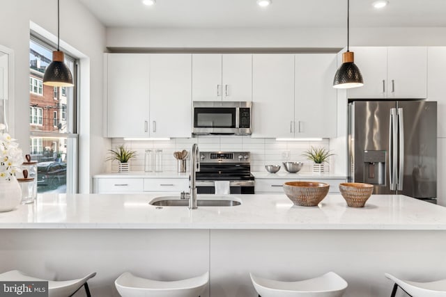 kitchen with appliances with stainless steel finishes, a breakfast bar, decorative light fixtures, sink, and white cabinets