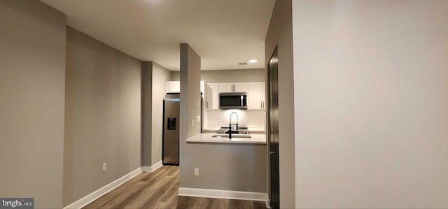 kitchen featuring sink, hardwood / wood-style flooring, appliances with stainless steel finishes, tasteful backsplash, and white cabinets