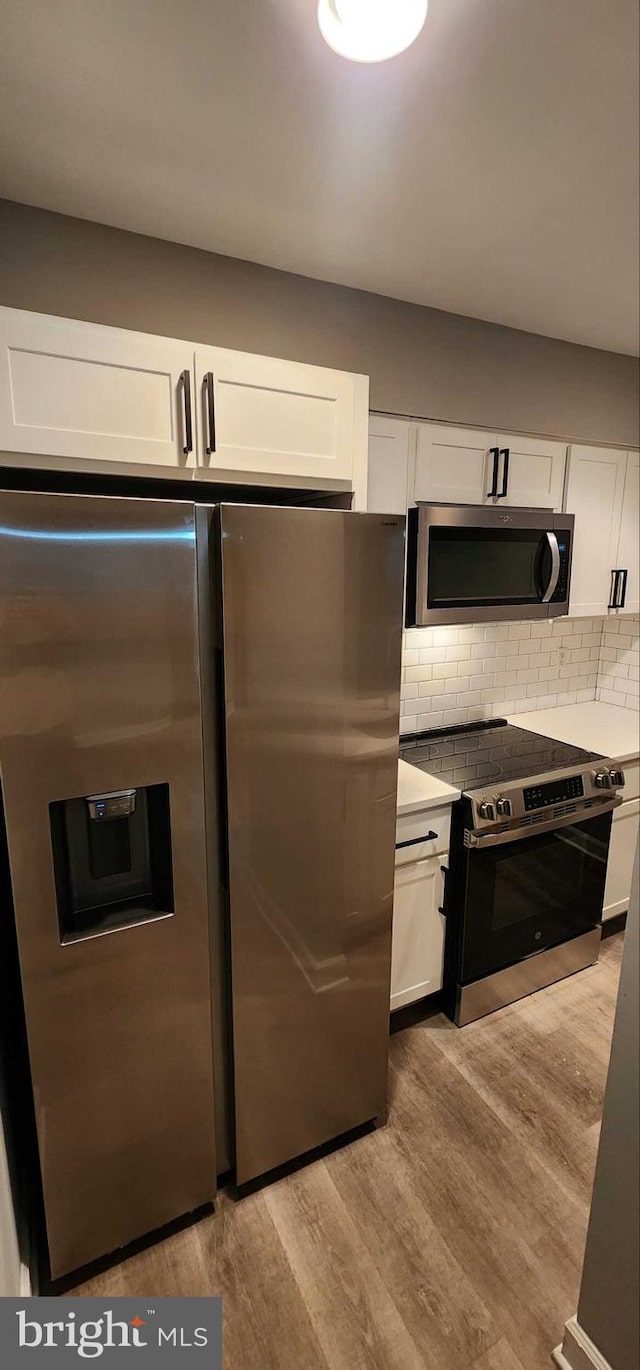 kitchen with tasteful backsplash, stainless steel appliances, light hardwood / wood-style floors, and white cabinets