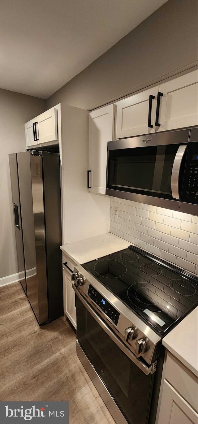 kitchen with white cabinetry, backsplash, stainless steel appliances, and light wood-type flooring